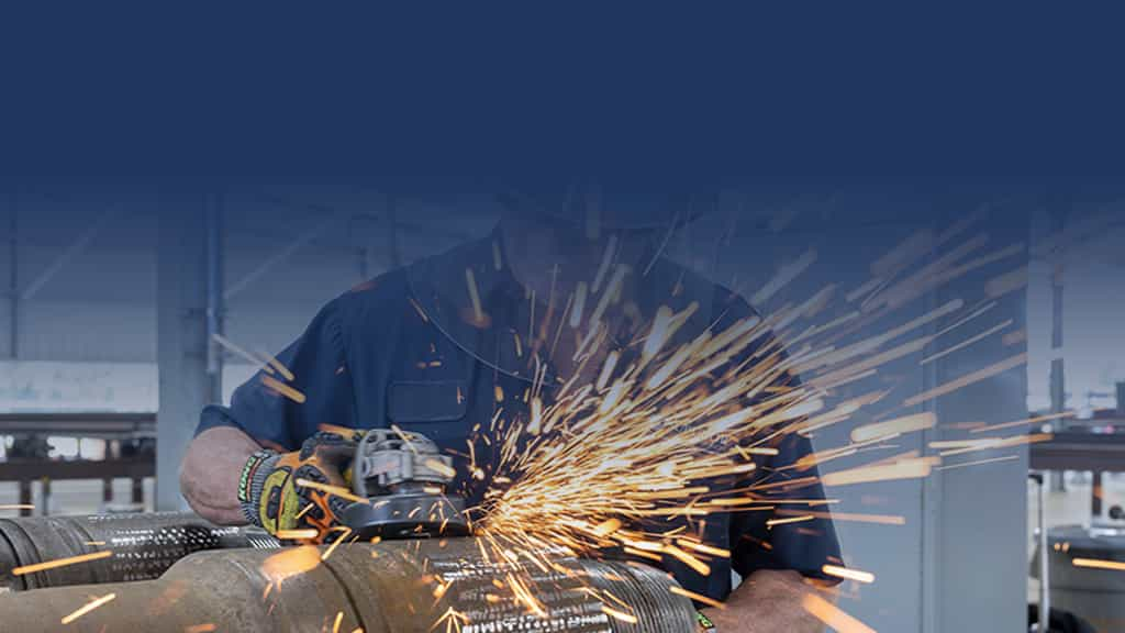 Man with face shield working on pipe with sparks flying