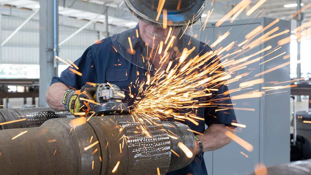 Man with face shield working on pipe with sparks flying